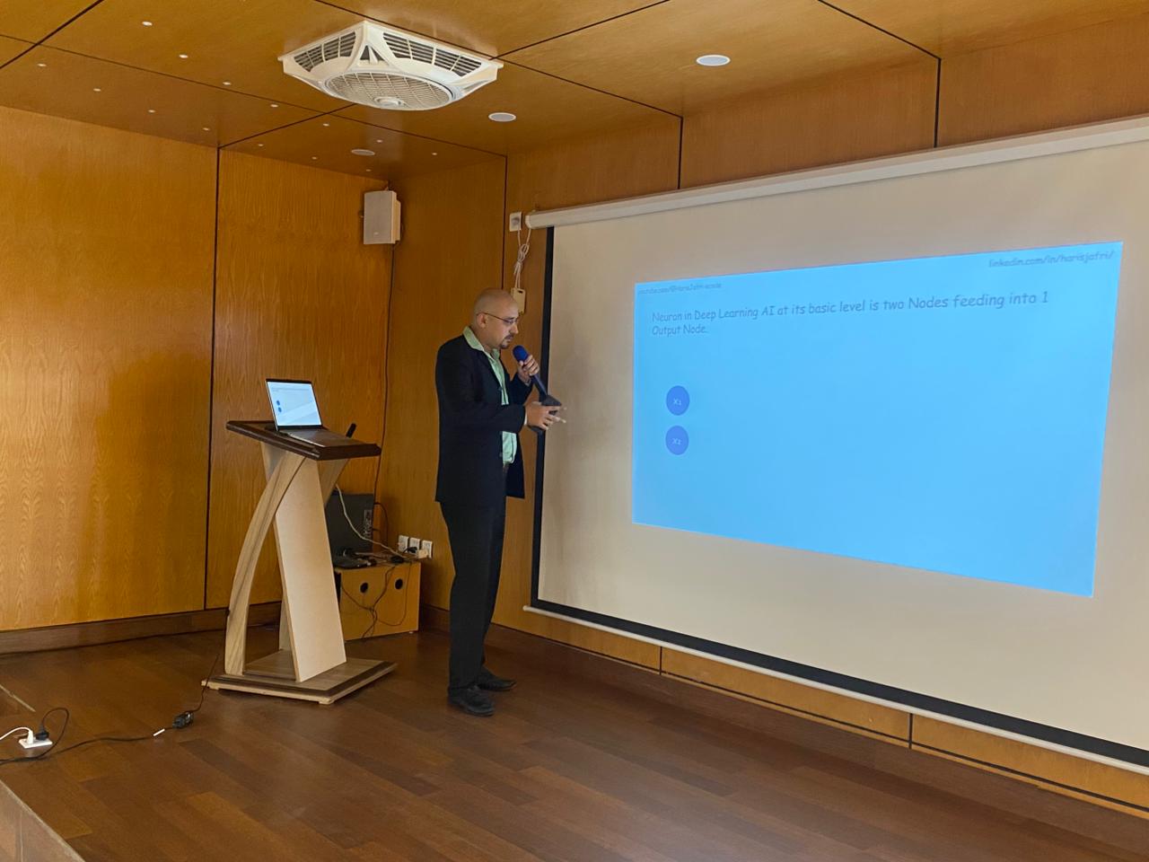 Haris Jafri presenting neural network node architecture at an auditorium podium